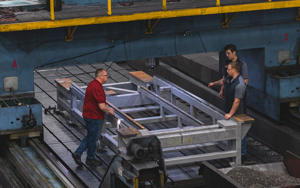 Three employees stand next to a large, rectangular metal fabricated piece.