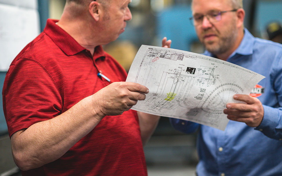 Two employees look at a CNC machine diagram.