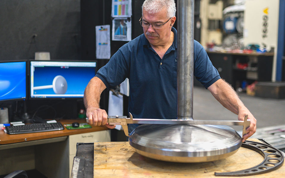 An employee measures an large, round metal disc with an instrument.