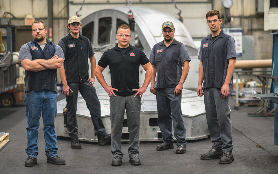 Five employees standing in front a very large machined piece.