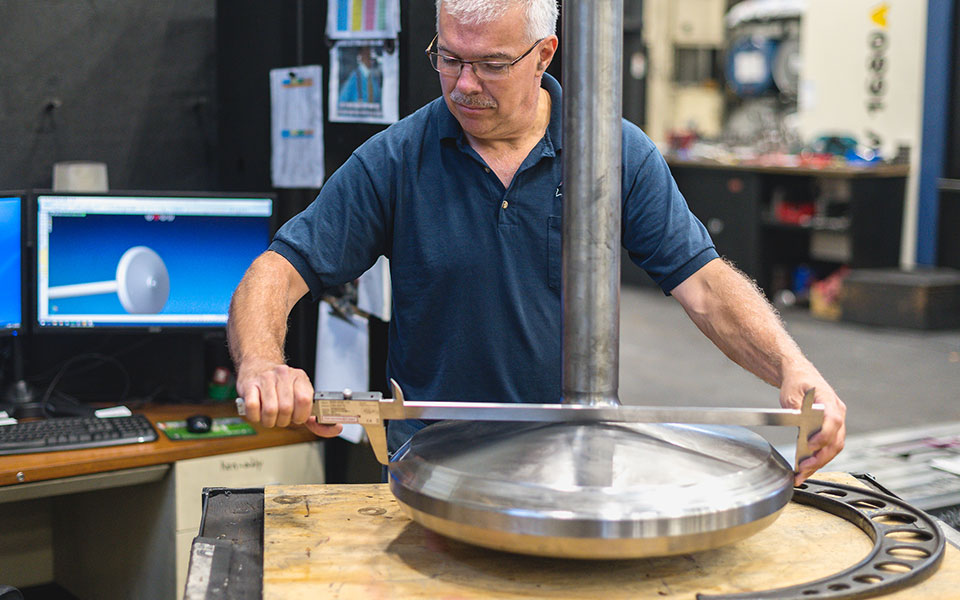 An employee measures a large round cylinder with a precise measurement device.