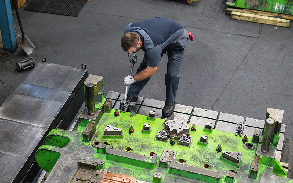 An employee works on a very large metal fabrication piece in green paint.