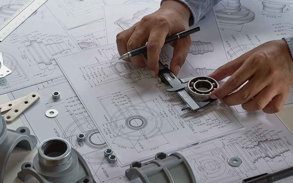 Hands measure the size of a metal ring on blueprints.